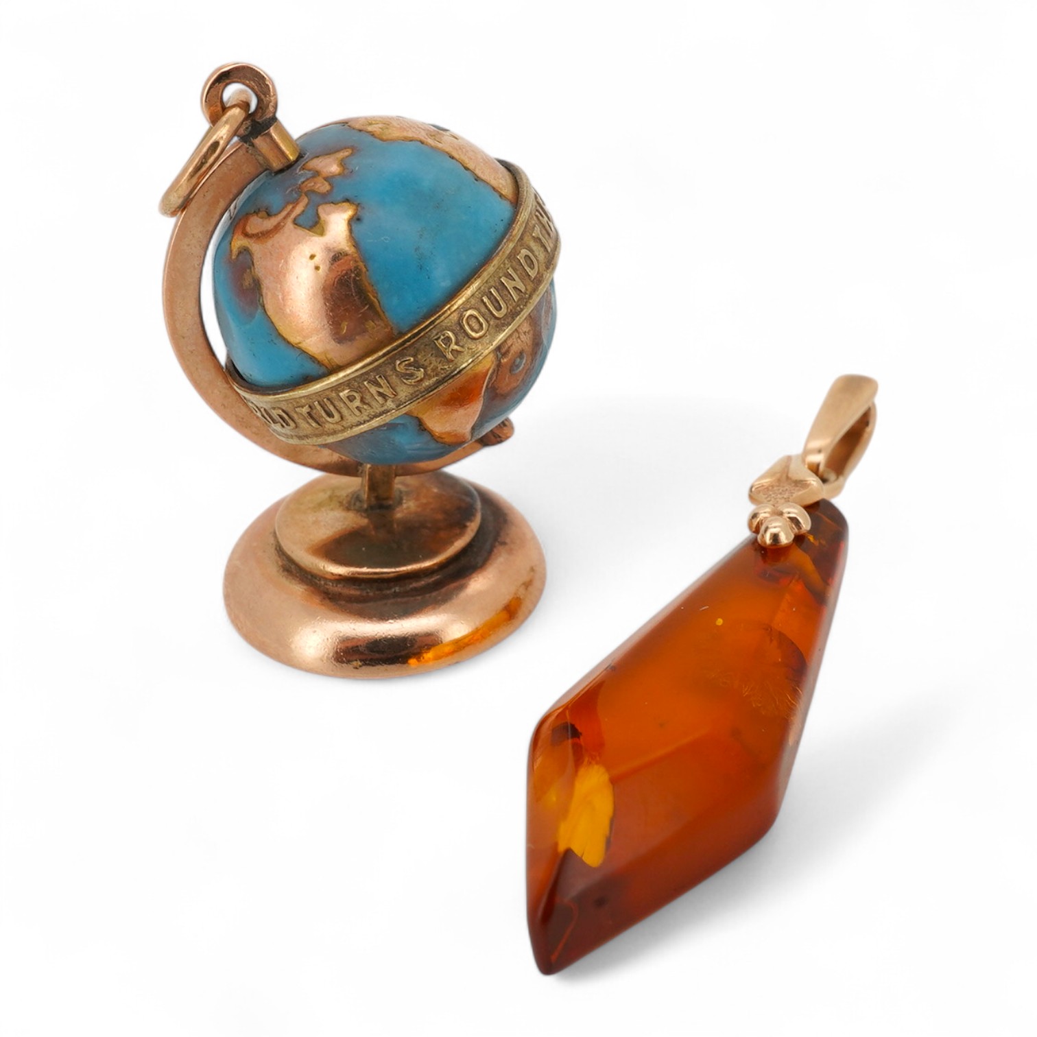 A yellow metal and enamel globe charm, reading 'The whole world turns round the love', height 3.2cm; and a gold and amber pendant, length 4.5cm, Russian assay marks for 14ct gold